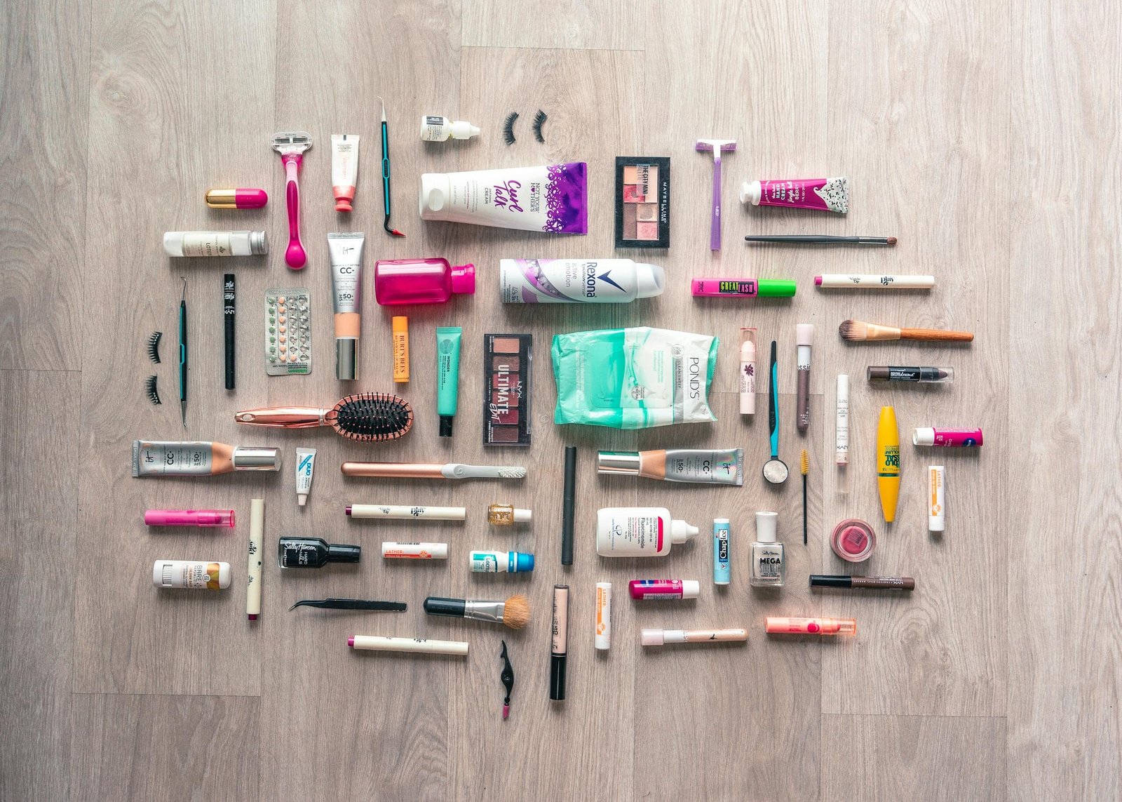 A diverse collection of beauty and grooming products neatly arranged on a wooden surface in a flatlay style.